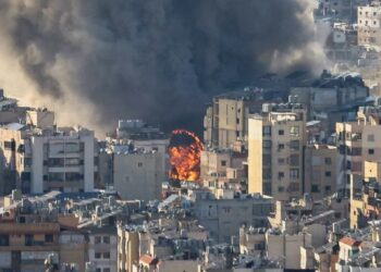 Prédios altos próximos a incêndio intenso com fumaça densa subindo no céu.
