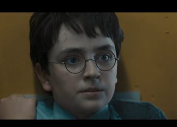 Harry Potter usando óculos redondos encara algo em ambiente iluminado