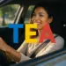 Mulher sorridente dirigindo um carro com as letras TEA coloridas na frente.