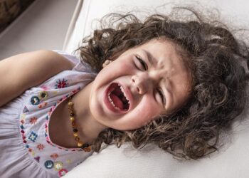 Menina de cabelo cacheado chorando deitada no sofá com expressão de frustração