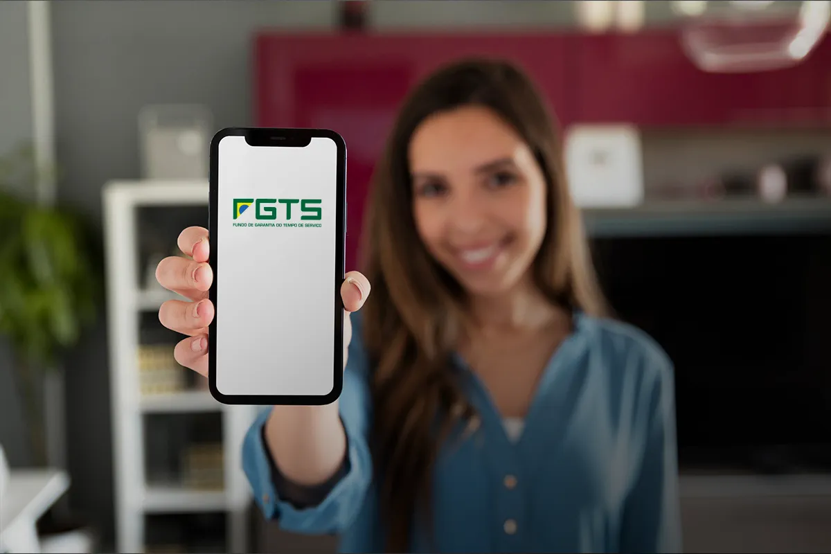 Saque do FGTS: novos brasileiros são contemplados com o valor de R$ 6.220 2 Mulher sorridente exibe celular com logotipo do FGTS na tela em sua casa.