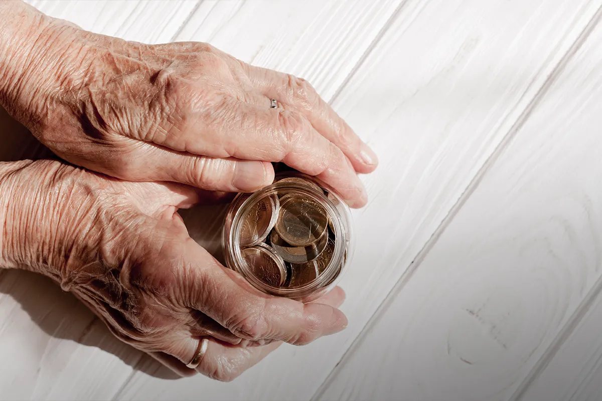 Seu CNIS pode ter erros e você nem sabe: veja como isso afeta o INSS 2 Mãos envelhecidas seguram pote de moedas europeias apoiado em superfície de madeira branca.