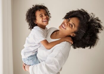 Mulher sorrindo enquanto segura criança que retribui o sorriso, ambos próximos e felizes.
