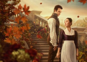 Um homem elegante com colete dourado e uma mulher com vestido de época bordô e avental branco trocam olhares em uma escadaria de pedra adornada com flores e folhas de outono alaranjadas.