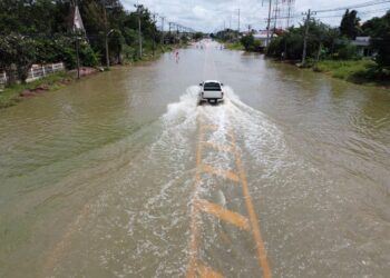 Carro atravessa via alagada após chuvas intensas em área urbana com risco de enchentes.