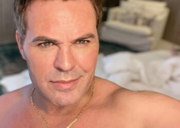Eduardo Costa exibe expressão séria e confiante em ambiente doméstico, usando colar dourado