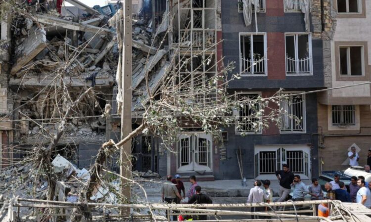 Guerra total no Oriente Médio: EUA e Israel atacam o Irã e os impactos são globais 1 Prédio parcialmente destruído após ataque, com escombros espalhados e moradores observando os danos em área urbana no Oriente Médio.