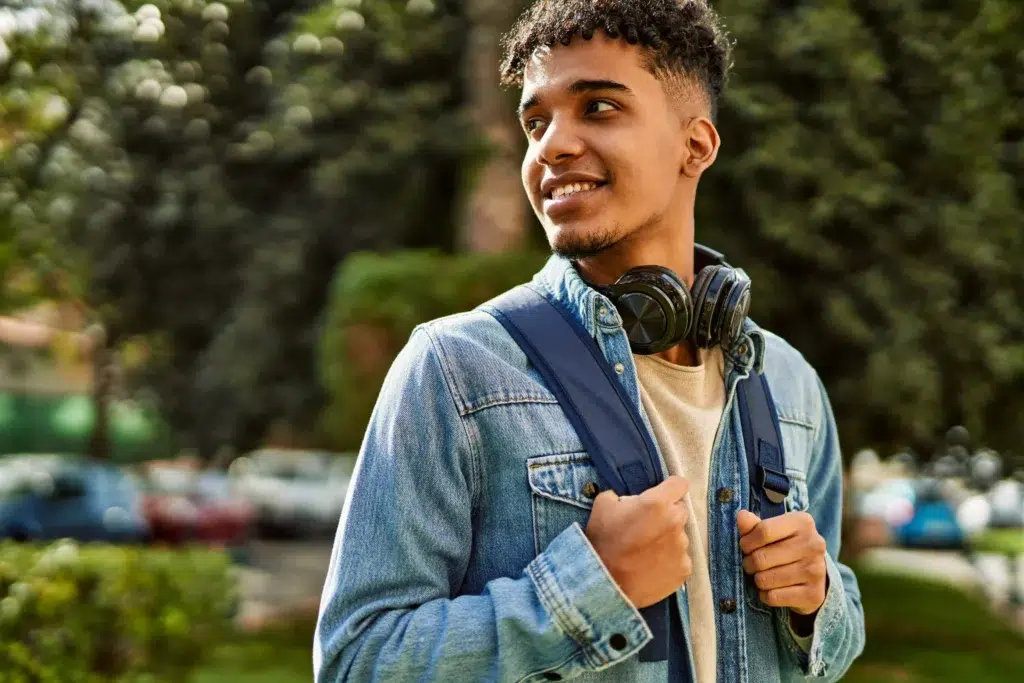 Nova lista de espera do Fies 2026 é liberada para consulta 2 Estudante sorrindo ao ar livre com mochila e fones no pescoço