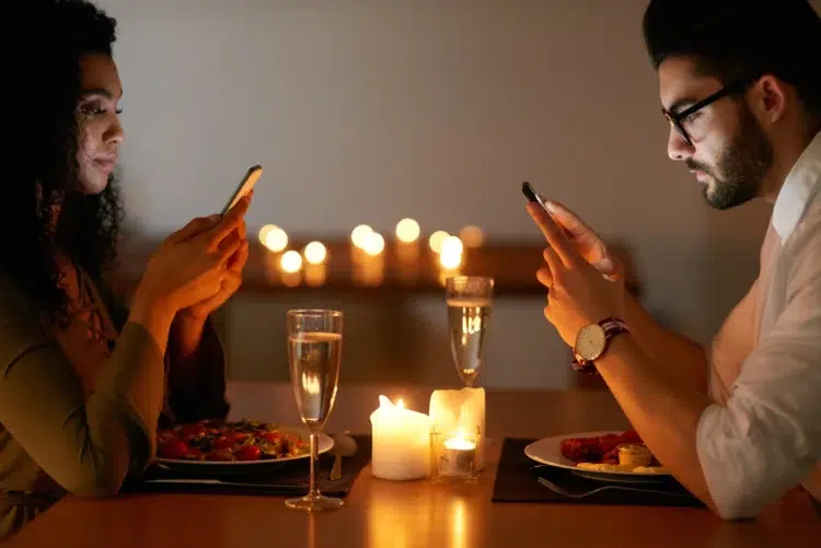O motivo oculto pelo qual casais estão parando de conversar em restaurantes 2 Duas pessoas sentadas à mesa de restaurante usando celulares, jantar à luz de velas