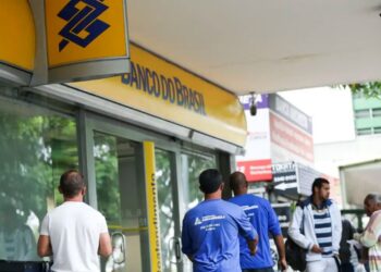 Fachada externa de uma agência do Banco do Brasil com pessoas caminhando na calçada em frente à entrada.