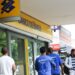 Fachada externa de uma agência do Banco do Brasil com pessoas caminhando na calçada em frente à entrada.