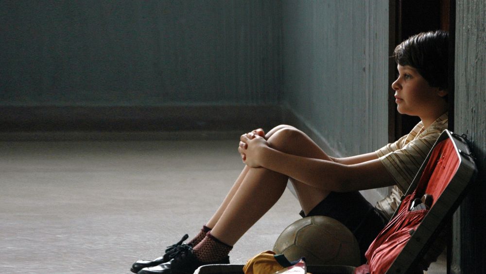 Vai fazer o Enem? Confira filmes brasileiros que tratam de temas sociais que podem aparecer na prova 4 O menino Mauro, protagonista do filme, sentado no chão abraçando os joelhos ao lado de uma mala e uma bola de futebol.