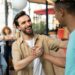 Dois homens sorridentes em um ambiente externo de confraternização, apertando as mãos de forma amigável enquanto conversam, com outras pessoas ao fundo.