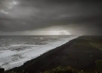 Nuvens escuras cobrem a praia enquanto ondas grandes atingem a faixa de areia escura