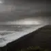 Nuvens escuras cobrem a praia enquanto ondas grandes atingem a faixa de areia escura