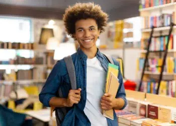 Estudante sorridente com mochila e cadernos em livraria iluminada
