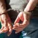 Caso de estupro coletivo contra menina de 17 anos no RJ: saiba quais são os agravantes e as punições legais 13 Homem algemado com as mãos para trás vestindo camiseta cinza e jeans