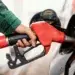 Mão segurando bico vermelho abastecendo carro preto em posto de combustível