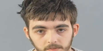 Carlo Tritta, 19 anos , em foto de custódia com cabelo castanho bagunçado, barba rala, expressão neutra e camiseta cinza.